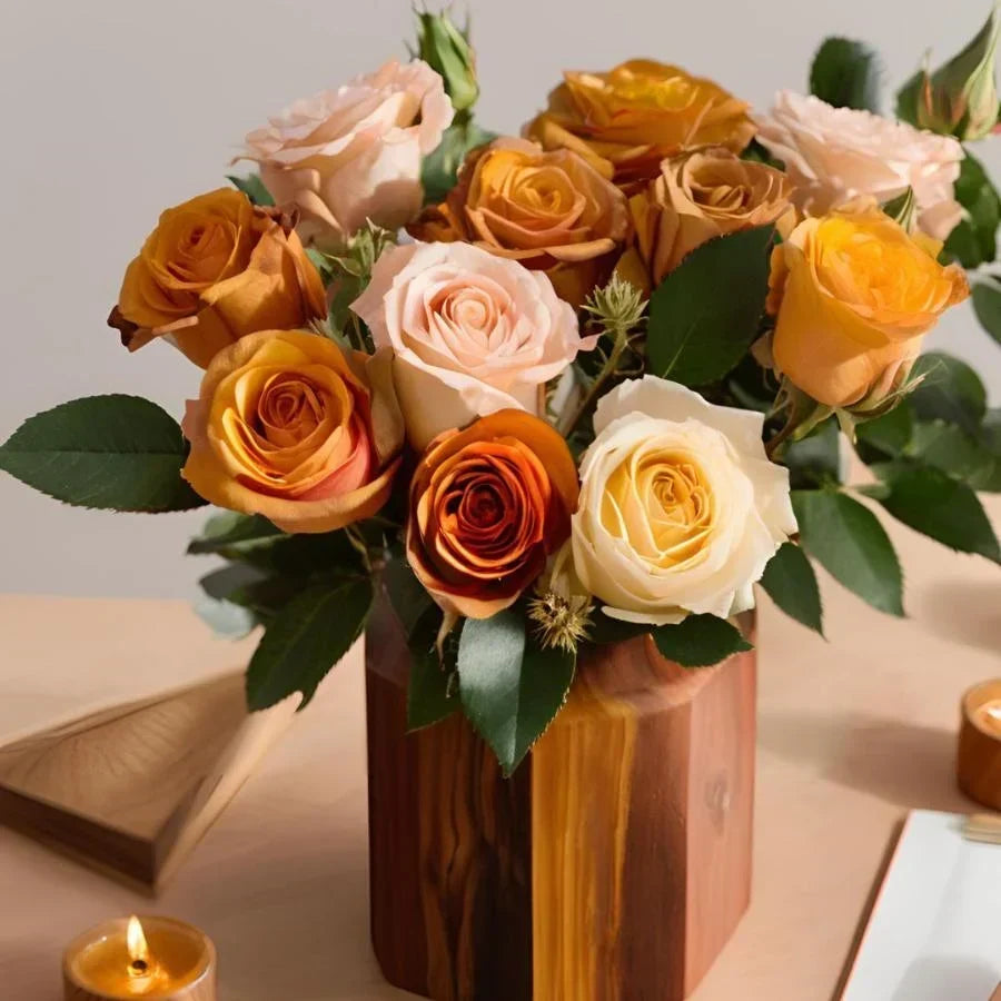 Sandalwood Rose: Orange, blush and cream roses arranged in a wooden vase beside a lit candle.