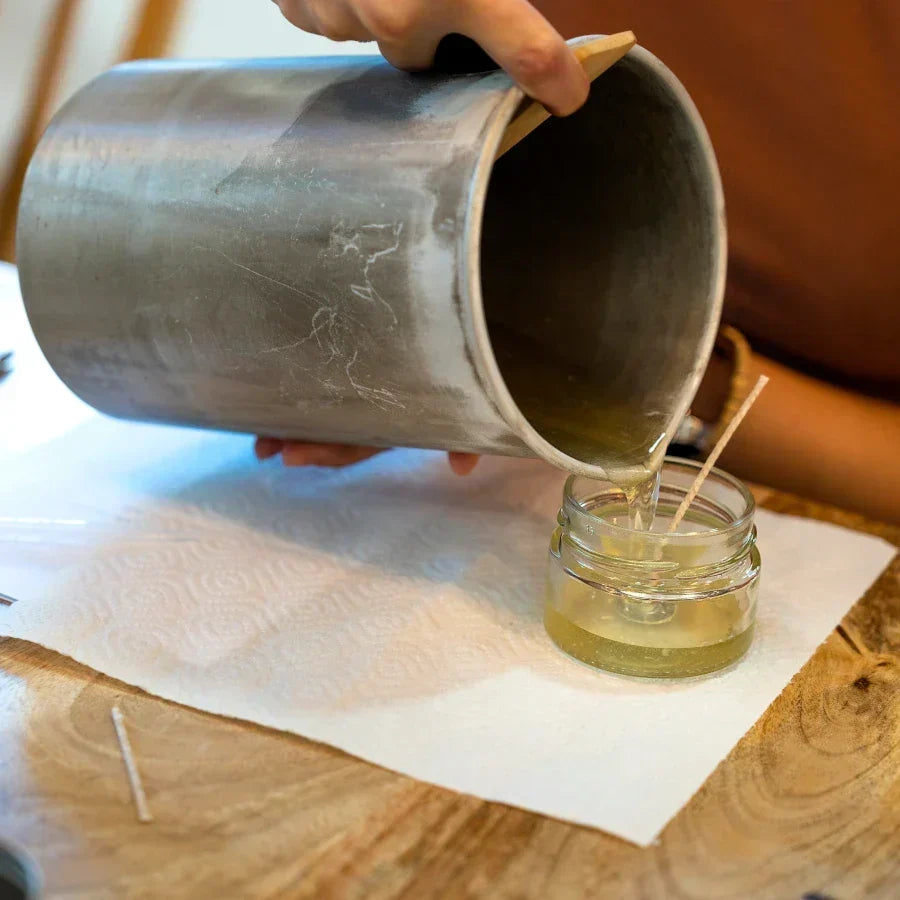 Candle maker pouring melted wax into a glass jar during a small fragrance oil test batch