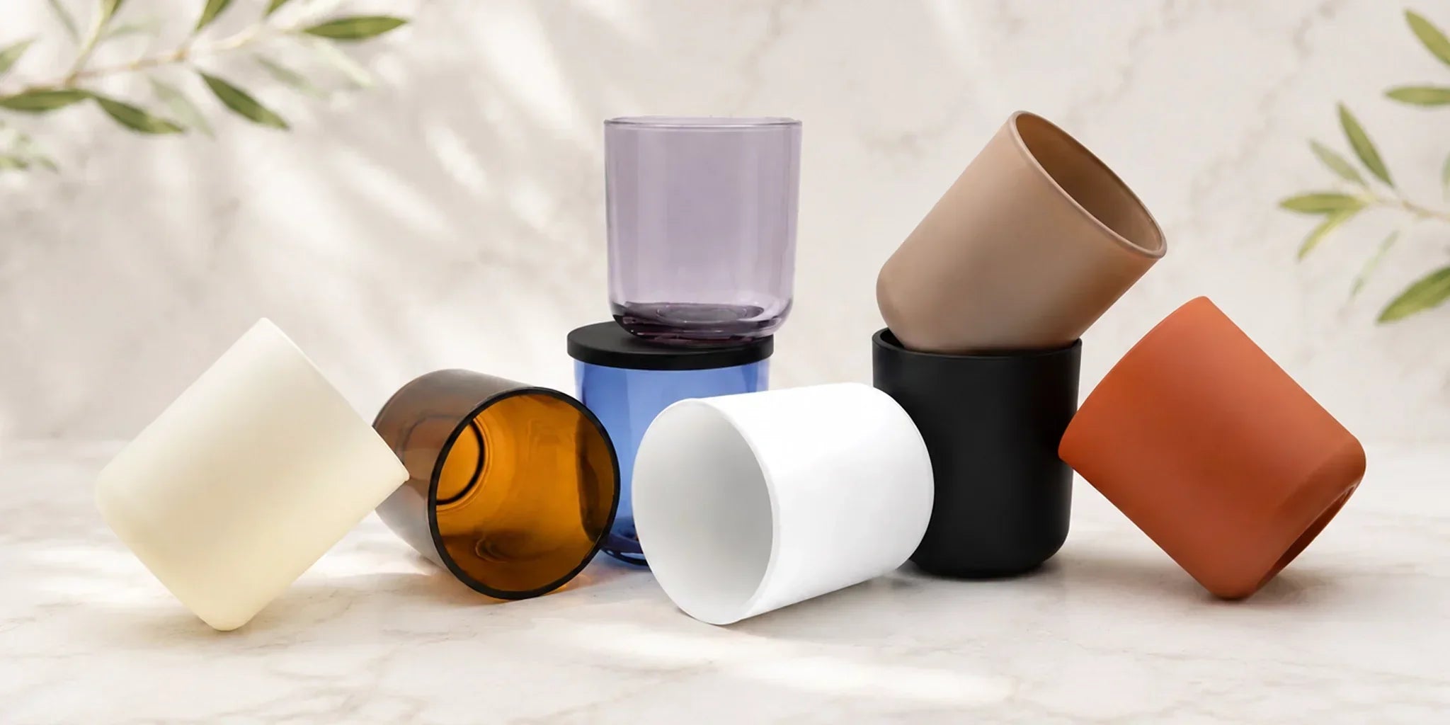 Assortment of candle-making containers and vessels in various shapes, sizes, and colors arranged on a light surface, showcasing options for candles and home fragrance products.